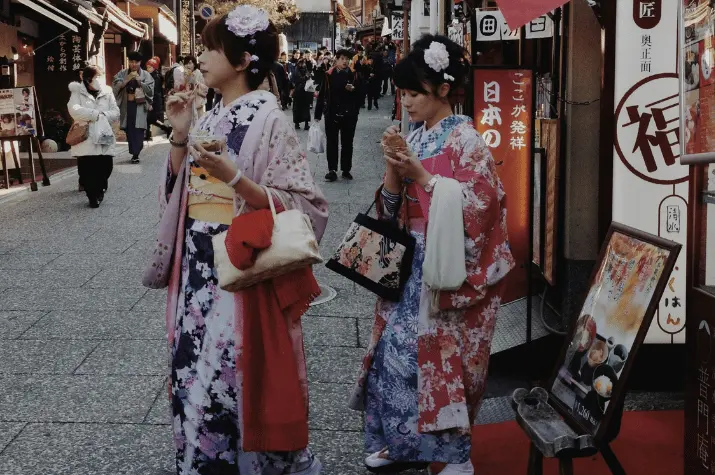Two women in traditional kimonos walking and enjoying street food in Japan