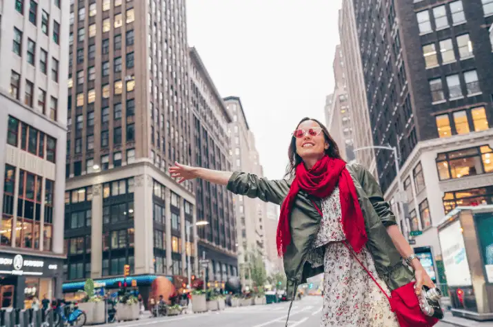 Woman smiling and walking on a city street with tall buildings in the background.