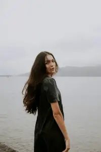 Woman with long hair in a black dress standing on the edge of the coast.
