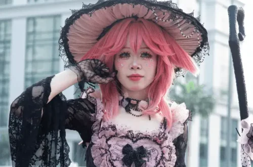 Professional cosplay photography featuring gothic lolita fashion with pink hair, ornate black dress, decorative hat, and detailed vintage-inspired accessories Caption: Stunning gothic lolita cosplay showcasing intricate Victorian-inspired fashion and artistic styling.