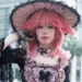 Professional cosplay photography featuring gothic lolita fashion with pink hair, ornate black dress, decorative hat, and detailed vintage-inspired accessories Caption: Stunning gothic lolita cosplay showcasing intricate Victorian-inspired fashion and artistic styling.