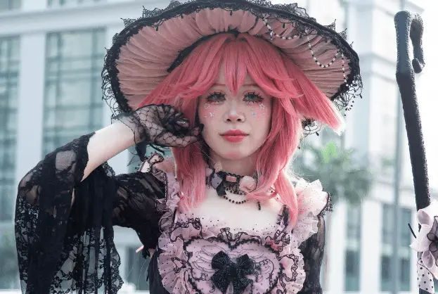 Professional cosplay photography featuring gothic lolita fashion with pink hair, ornate black dress, decorative hat, and detailed vintage-inspired accessories Caption: Stunning gothic lolita cosplay showcasing intricate Victorian-inspired fashion and artistic styling.