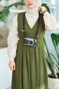 Modest fashion with a green pleated dress and vintage camera accessory