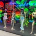Mannequins in rave-style outfits showcased in a shopfront with glowing graffiti art