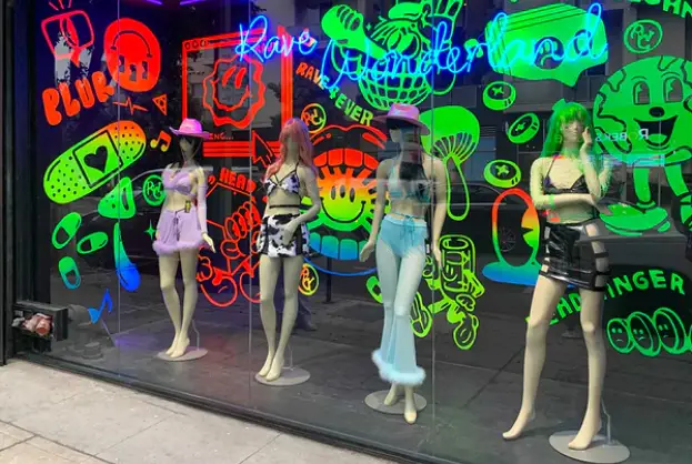 Mannequins in rave-style outfits showcased in a shopfront with glowing graffiti art