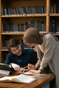 Two students engaged in a discussion with study materials in a library