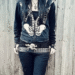 Person wearing emo fashion featuring black skeleton print hoodie, studded belt, dark jeans against weathered wood background